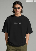 Person wearing a black t-shirt with 'KANYE' printed on it against a gray background