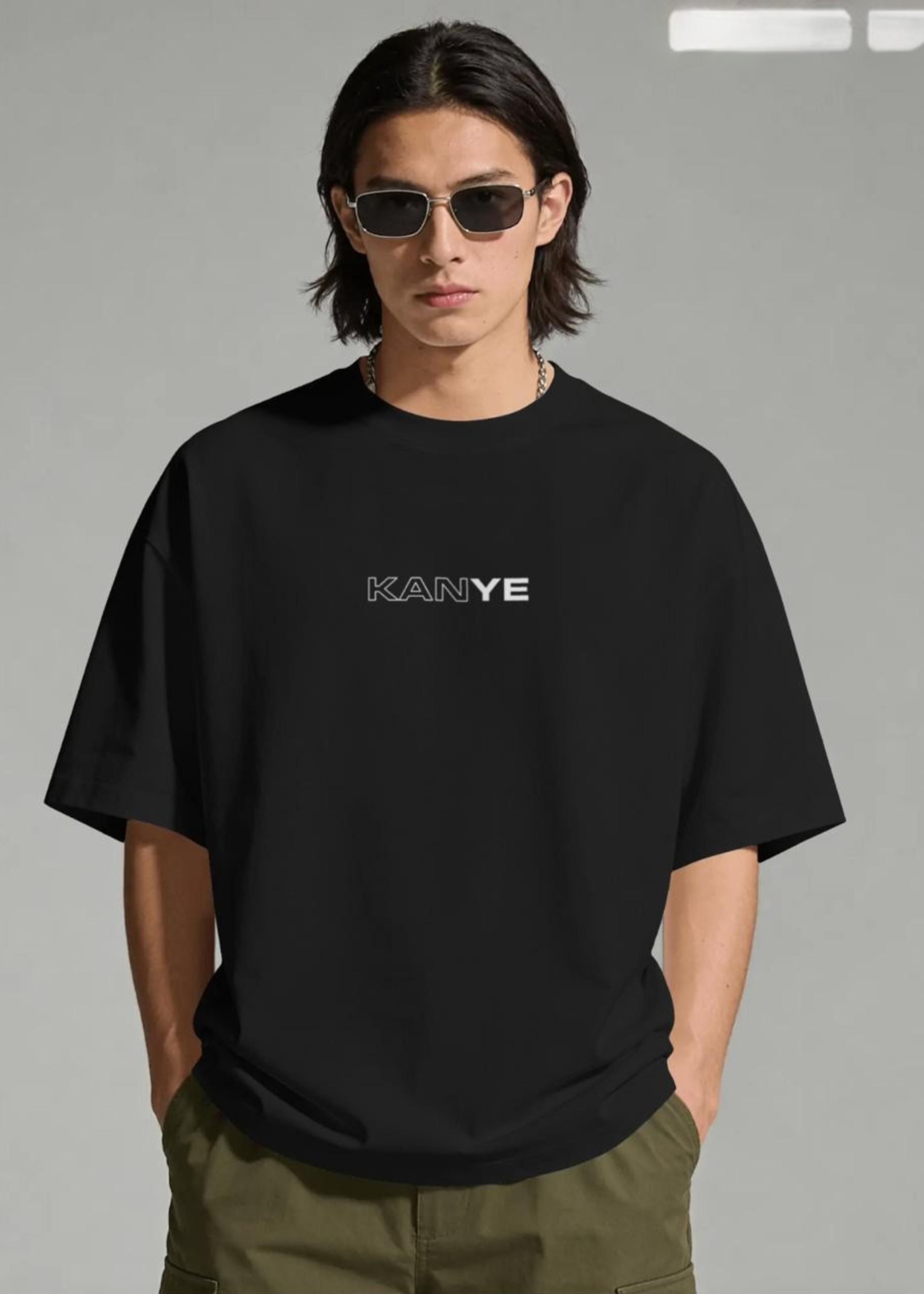 Person wearing a black t-shirt with 'KANYE' printed on it against a gray background
