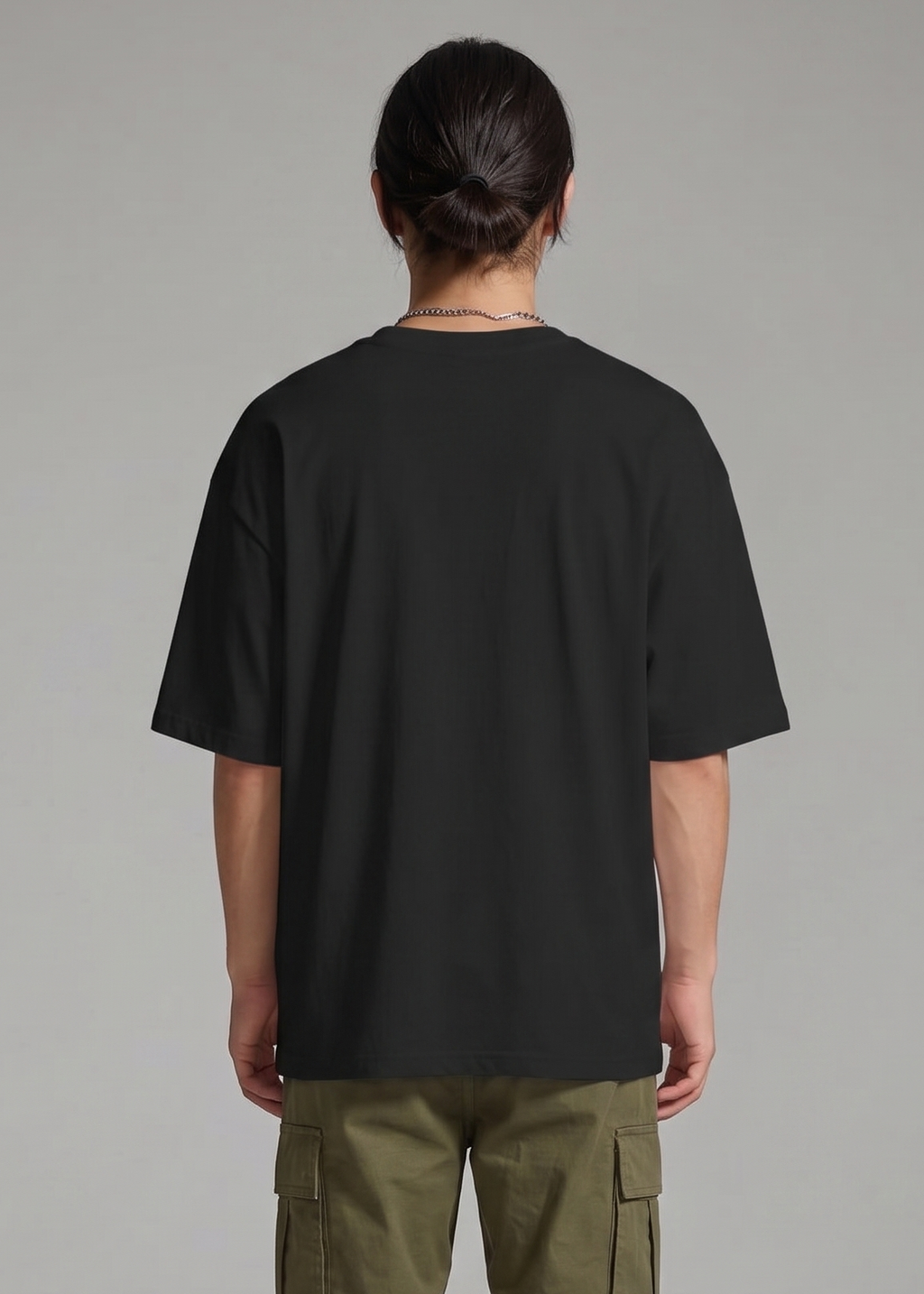 Person wearing a black oversized t-shirt and green cargo pants on a gray background
