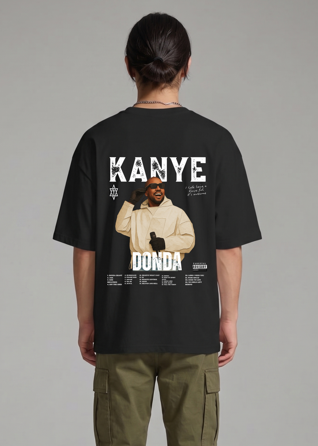 Person wearing a black t-shirt with 'Kanye' and 'Donda' graphic on the back, standing against a gray background.